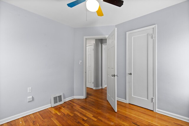 unfurnished bedroom featuring ceiling fan, wood finished floors, visible vents, and baseboards