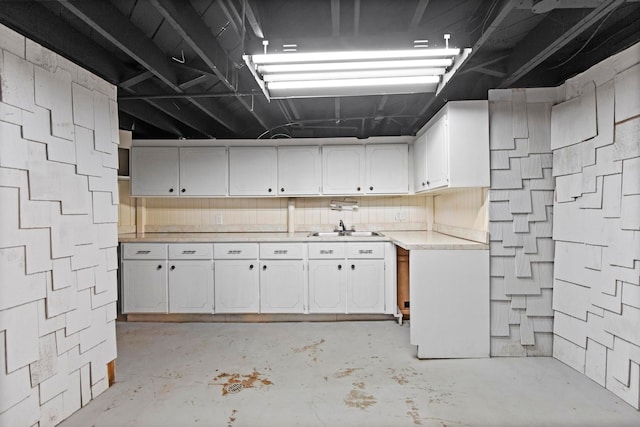 kitchen with white cabinetry, light countertops, unfinished concrete flooring, and a sink