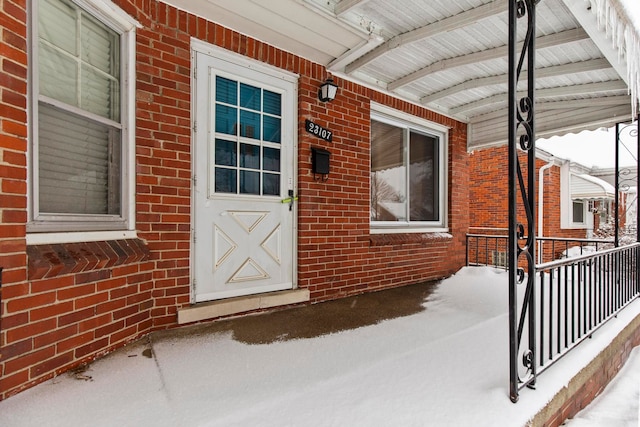 snow covered property entrance with covered porch and brick siding