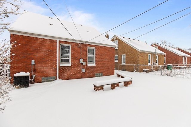 snow covered property with central AC unit, fence, and brick siding