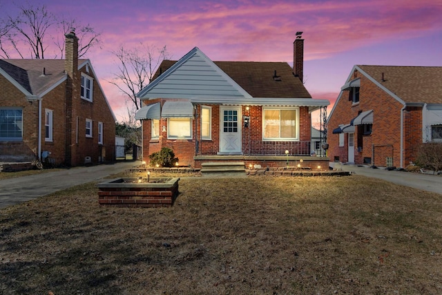 bungalow featuring a lawn, brick siding, and a chimney