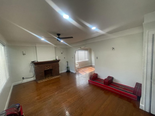 unfurnished living room with baseboards, arched walkways, a ceiling fan, wood finished floors, and a fireplace