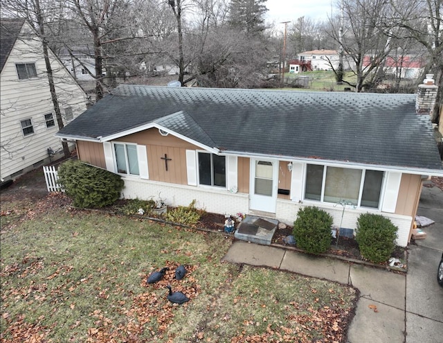 view of front of home featuring roof with shingles, brick siding, a chimney, and a front yard