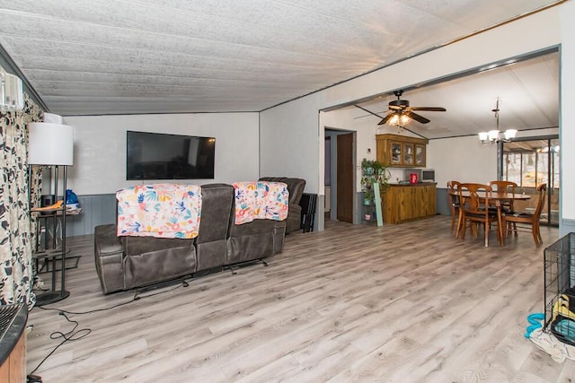 living area with vaulted ceiling, a wainscoted wall, ceiling fan with notable chandelier, and wood finished floors