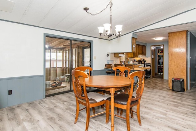 dining room with light wood-type flooring, wainscoting, vaulted ceiling, and a notable chandelier