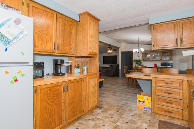 kitchen with brown cabinetry, freestanding refrigerator, light countertops, and ceiling fan with notable chandelier