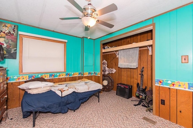 carpeted bedroom featuring wood walls, ceiling fan, and a closet