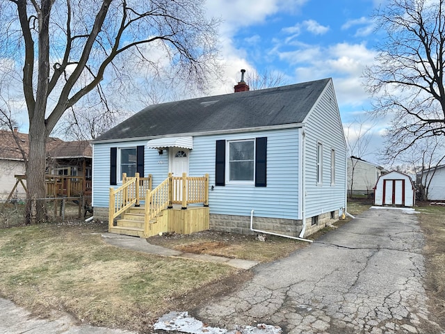 view of front of home featuring a shingled roof, a chimney, aphalt driveway, fence, and an outdoor structure