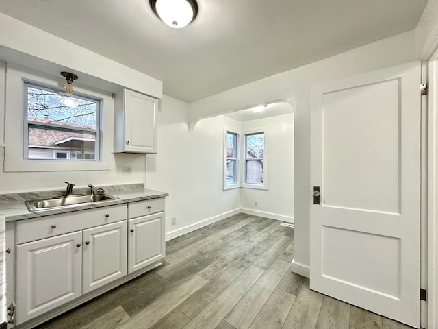 kitchen with light countertops, light wood-style floors, white cabinetry, a sink, and baseboards