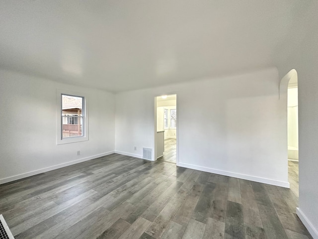 spare room with arched walkways, dark wood-style flooring, visible vents, and baseboards