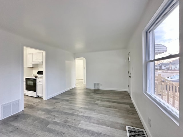 unfurnished living room featuring arched walkways, visible vents, baseboards, and wood finished floors