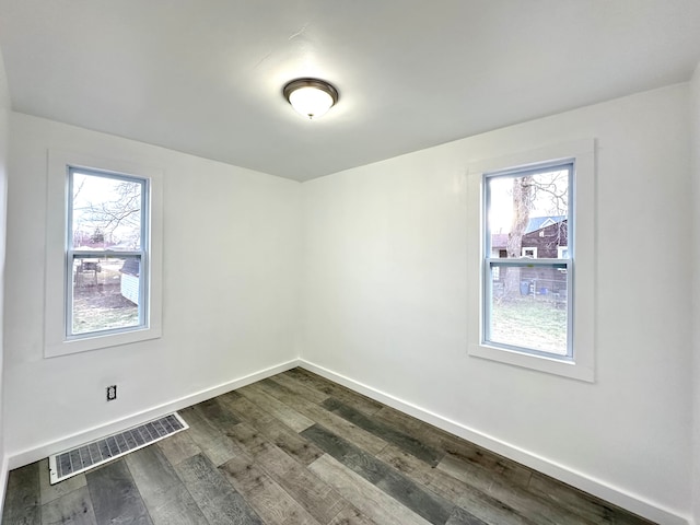 spare room with dark wood finished floors, visible vents, and baseboards