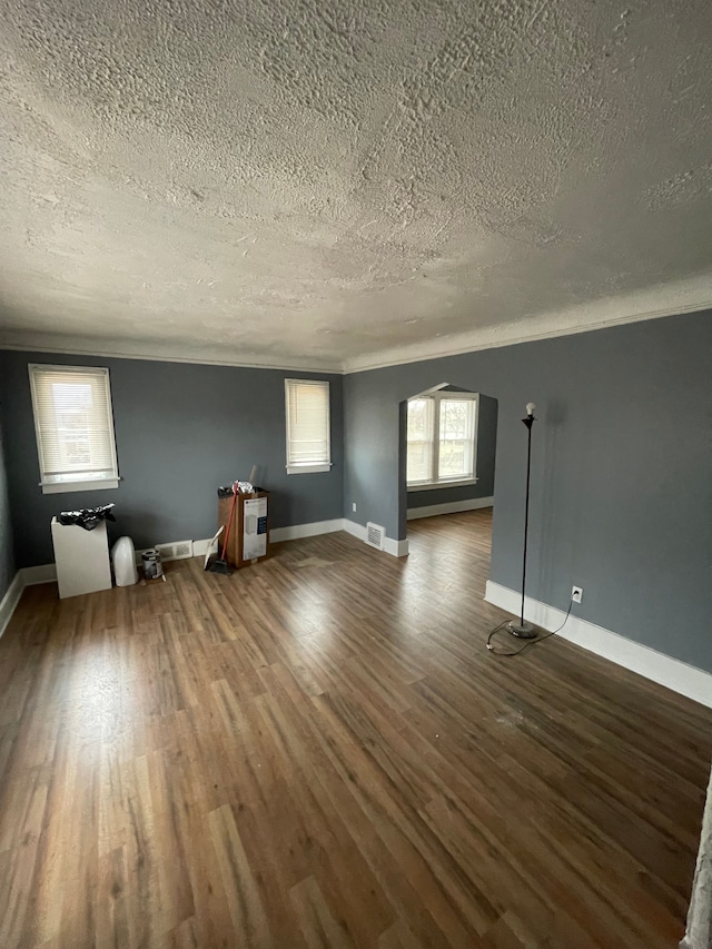 empty room featuring arched walkways, visible vents, baseboards, and wood finished floors