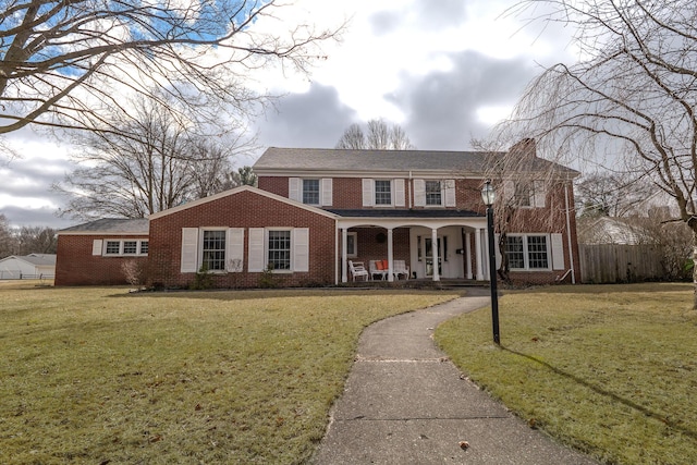 view of front of home featuring brick siding, fence, a porch, and a front yard