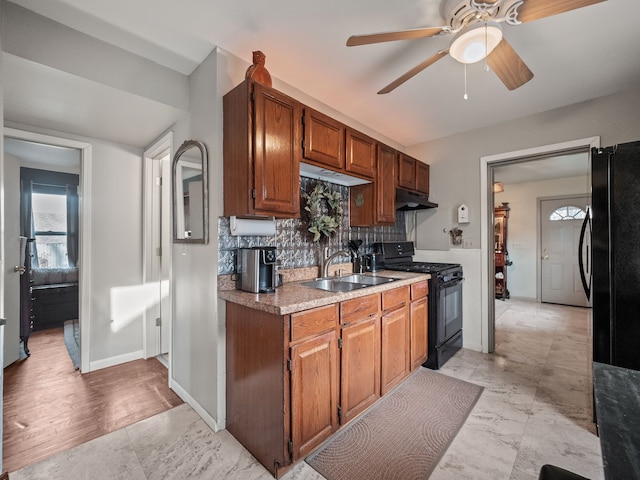 kitchen with backsplash, under cabinet range hood, light countertops, black appliances, and a sink