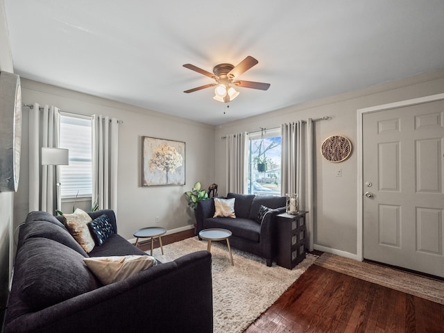 living room featuring baseboards, a ceiling fan, and dark wood-style flooring