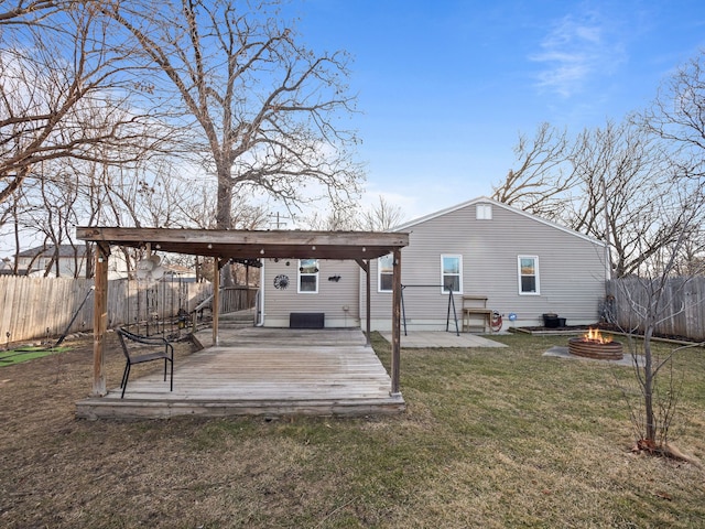 back of property featuring a wooden deck, an outdoor fire pit, a fenced backyard, a yard, and a patio