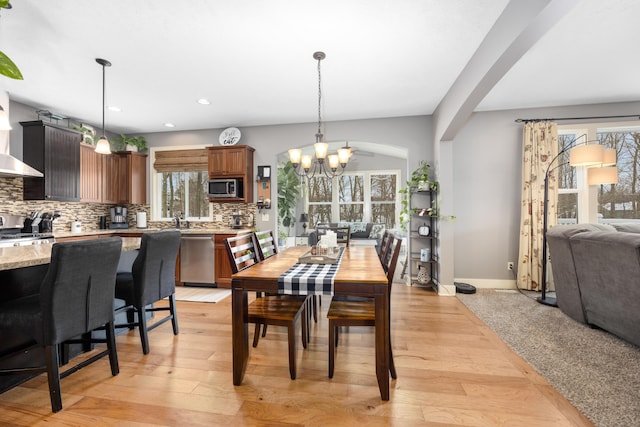 dining area featuring arched walkways, light wood-style flooring, recessed lighting, baseboards, and an inviting chandelier