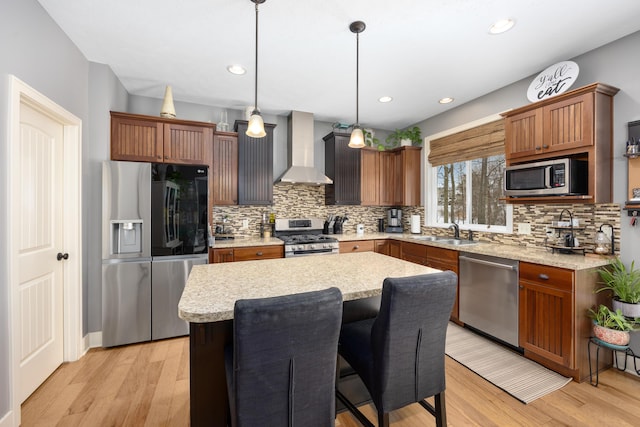 kitchen featuring wall chimney range hood, stainless steel appliances, a sink, and light wood finished floors