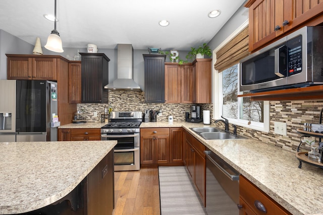 kitchen featuring light wood finished floors, light countertops, appliances with stainless steel finishes, a sink, and wall chimney exhaust hood