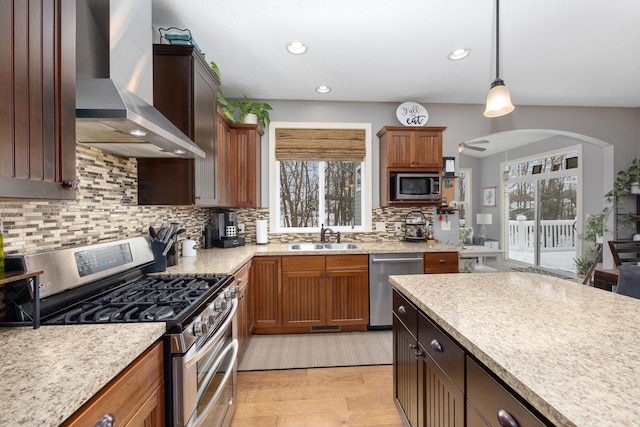 kitchen with wall chimney exhaust hood, stainless steel appliances, light wood-style floors, pendant lighting, and a sink