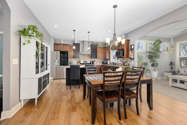 dining space with arched walkways, light wood finished floors, recessed lighting, a chandelier, and baseboards