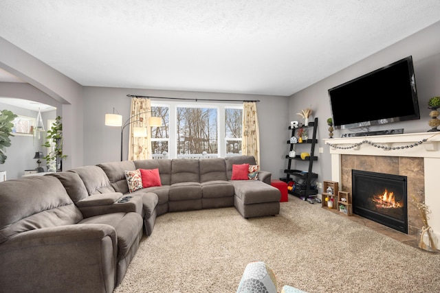 living area featuring a textured ceiling, carpet floors, a tiled fireplace, and arched walkways