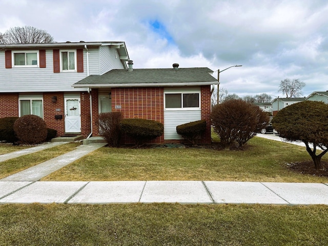 view of front of property with a shingled roof, a front yard, and brick siding