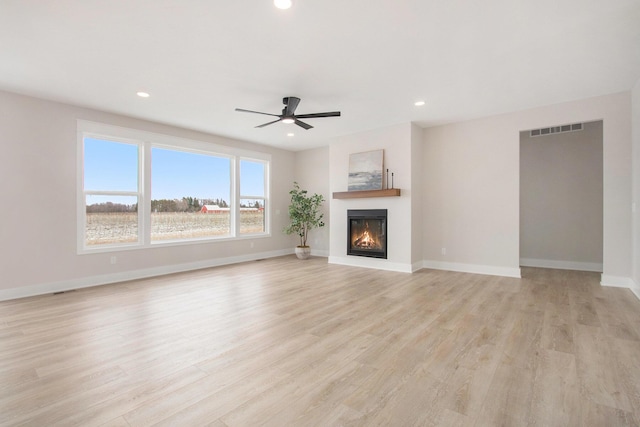 unfurnished living room with light wood finished floors, recessed lighting, a glass covered fireplace, and baseboards