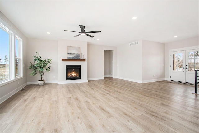 unfurnished living room featuring french doors, visible vents, light wood-style floors, a lit fireplace, and baseboards