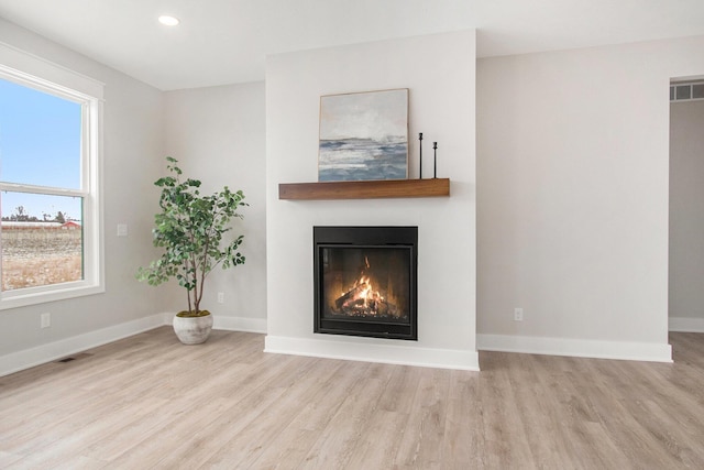 unfurnished living room with baseboards, wood finished floors, and a glass covered fireplace