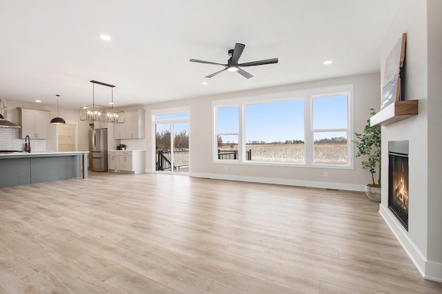 unfurnished living room with a warm lit fireplace, baseboards, and light wood finished floors