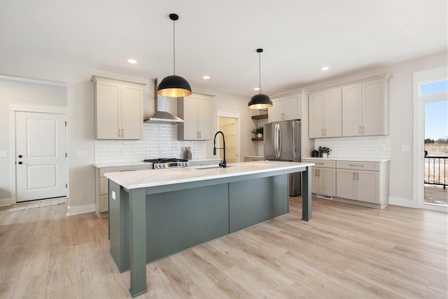 kitchen featuring light countertops, wall chimney range hood, a sink, and light wood-style floors