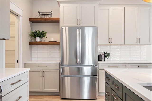 kitchen featuring freestanding refrigerator, light stone countertops, light wood-type flooring, open shelves, and backsplash