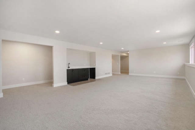 unfurnished living room with recessed lighting, visible vents, light carpet, wet bar, and baseboards