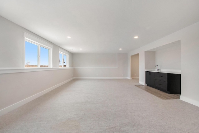 basement featuring recessed lighting, light colored carpet, a sink, baseboards, and wet bar