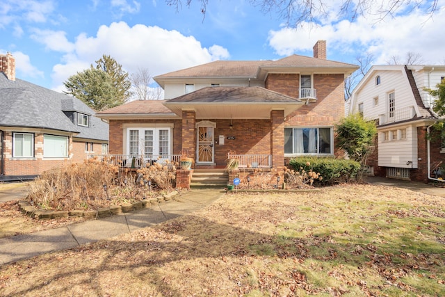 view of front of home with covered porch, a chimney, and brick siding