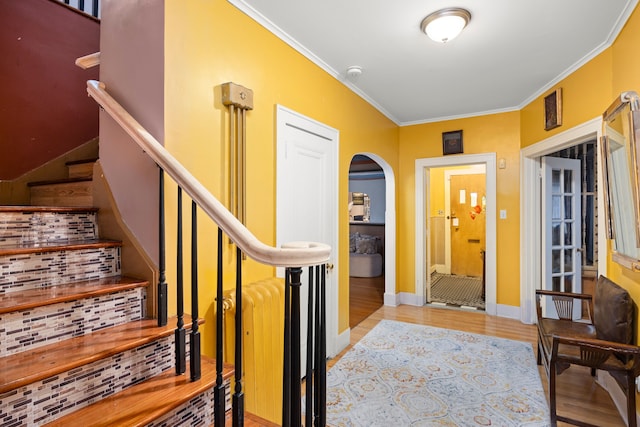 entryway featuring baseboards, arched walkways, ornamental molding, wood finished floors, and stairs