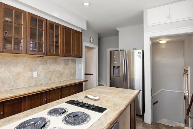 kitchen with white electric stovetop, tile counters, stainless steel fridge with ice dispenser, tasteful backsplash, and glass insert cabinets