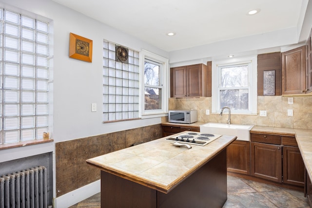 kitchen featuring tasteful backsplash, white electric stovetop, tile counters, radiator, and a sink