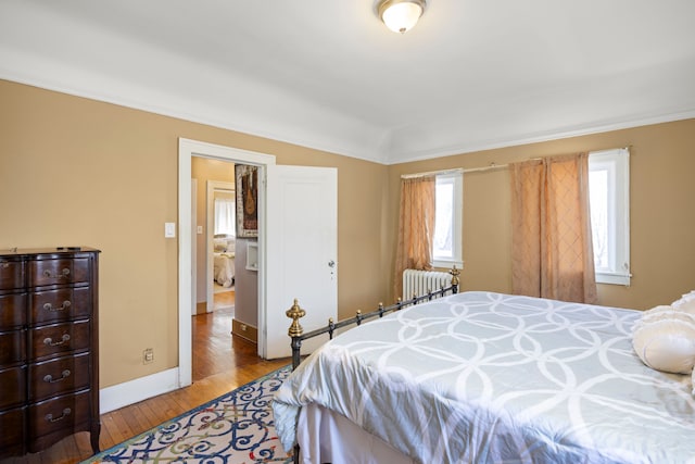 bedroom featuring radiator, vaulted ceiling, wood-type flooring, and baseboards