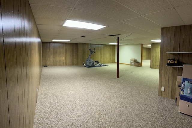 finished below grade area with a drop ceiling, carpet flooring, and wooden walls