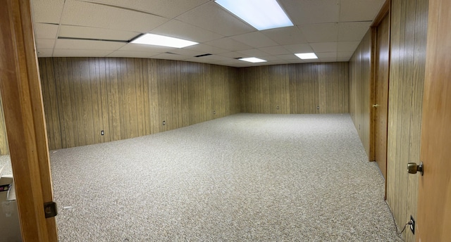 finished below grade area with wooden walls, a drop ceiling, and carpet flooring