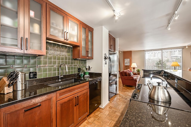 kitchen featuring black dishwasher, backsplash, freestanding refrigerator, a sink, and dark stone counters