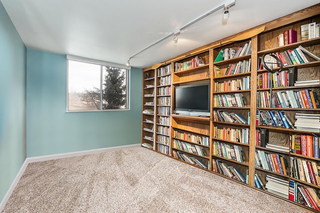 living area with bookshelves, track lighting, carpet flooring, and baseboards