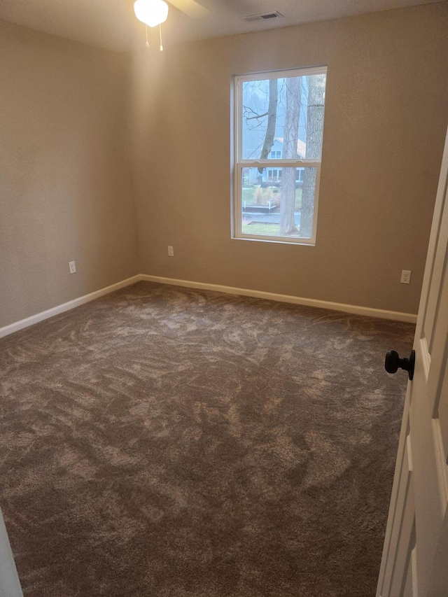unfurnished room featuring dark colored carpet, visible vents, and baseboards
