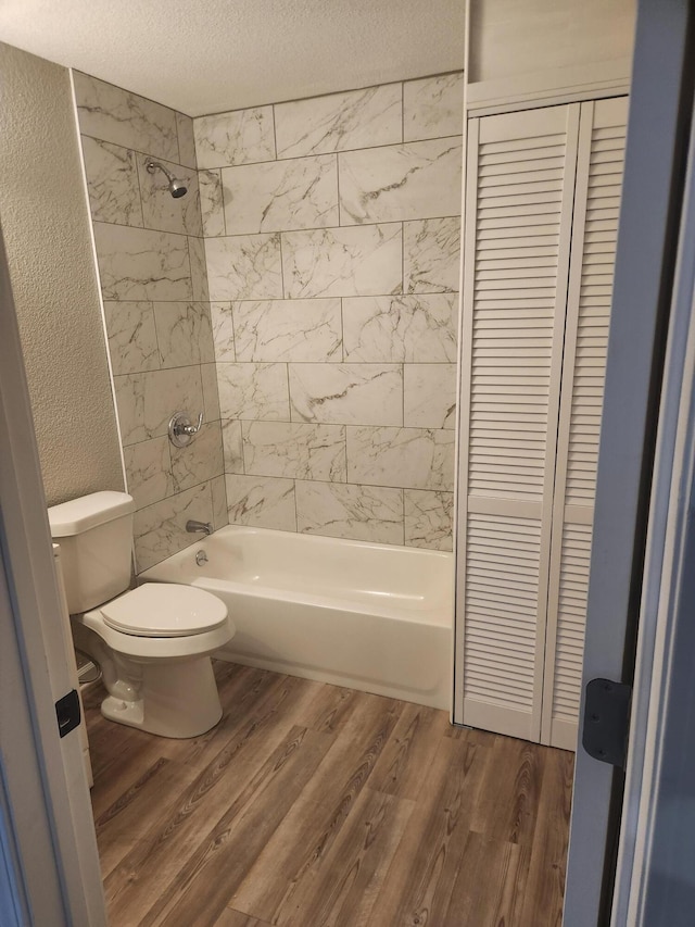 bathroom with a textured wall, toilet, wood finished floors,  shower combination, and a textured ceiling