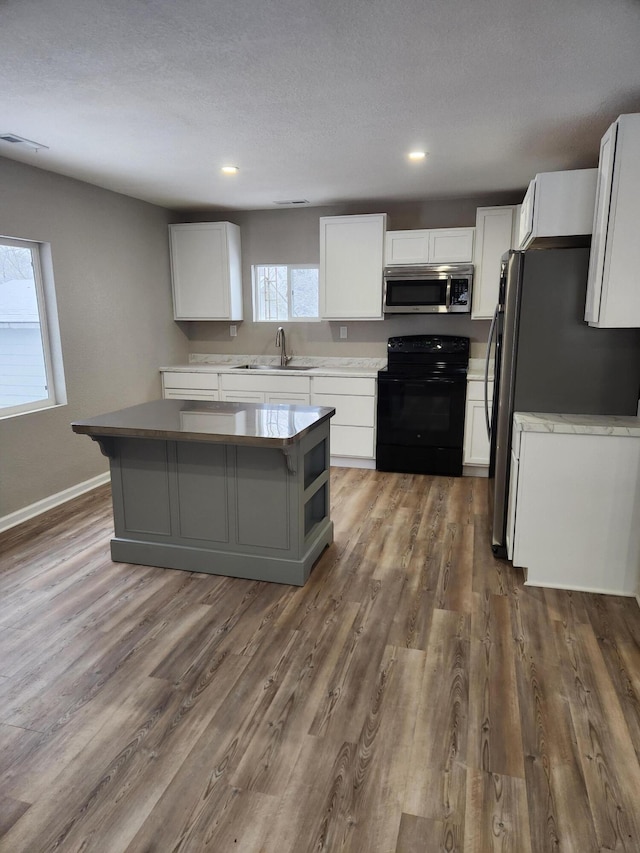 kitchen featuring visible vents, white cabinets, appliances with stainless steel finishes, wood finished floors, and a sink