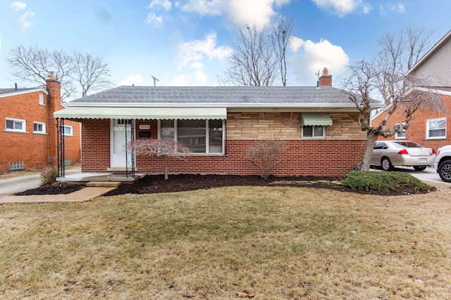 view of front facade with a shingled roof, a front yard, brick siding, and a chimney