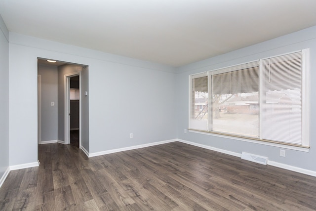 empty room featuring baseboards, visible vents, and dark wood finished floors